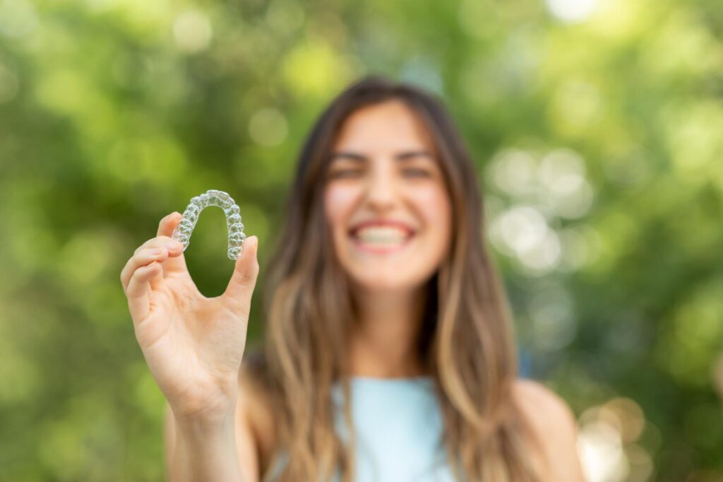 Teen girl holding up a clear aligner tray outdoors